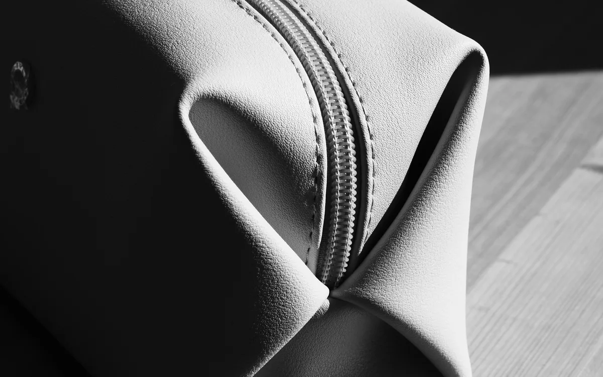 Close detail of a cream leather accessory and its zipper in soft directional light